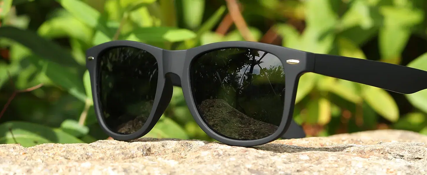 Black square-frame MEETSUN sunglasses resting on stone in front of green foliage