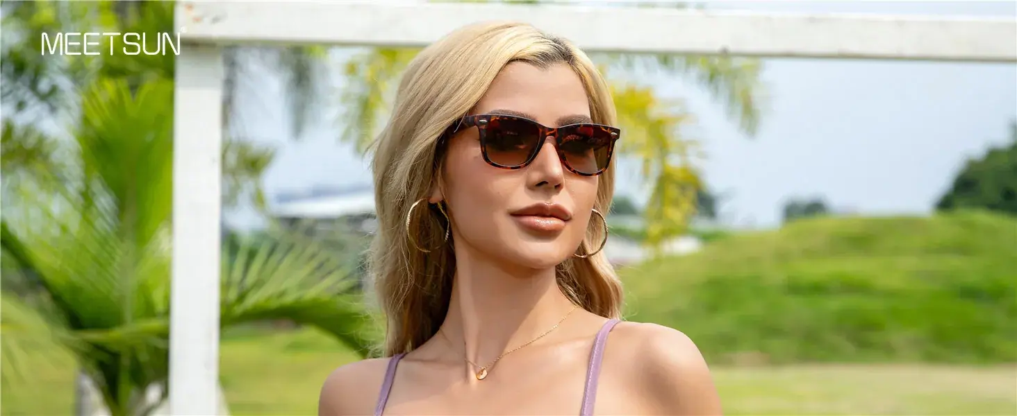 Woman wearing dark square-frame sunglasses in a sunny green outdoor setting